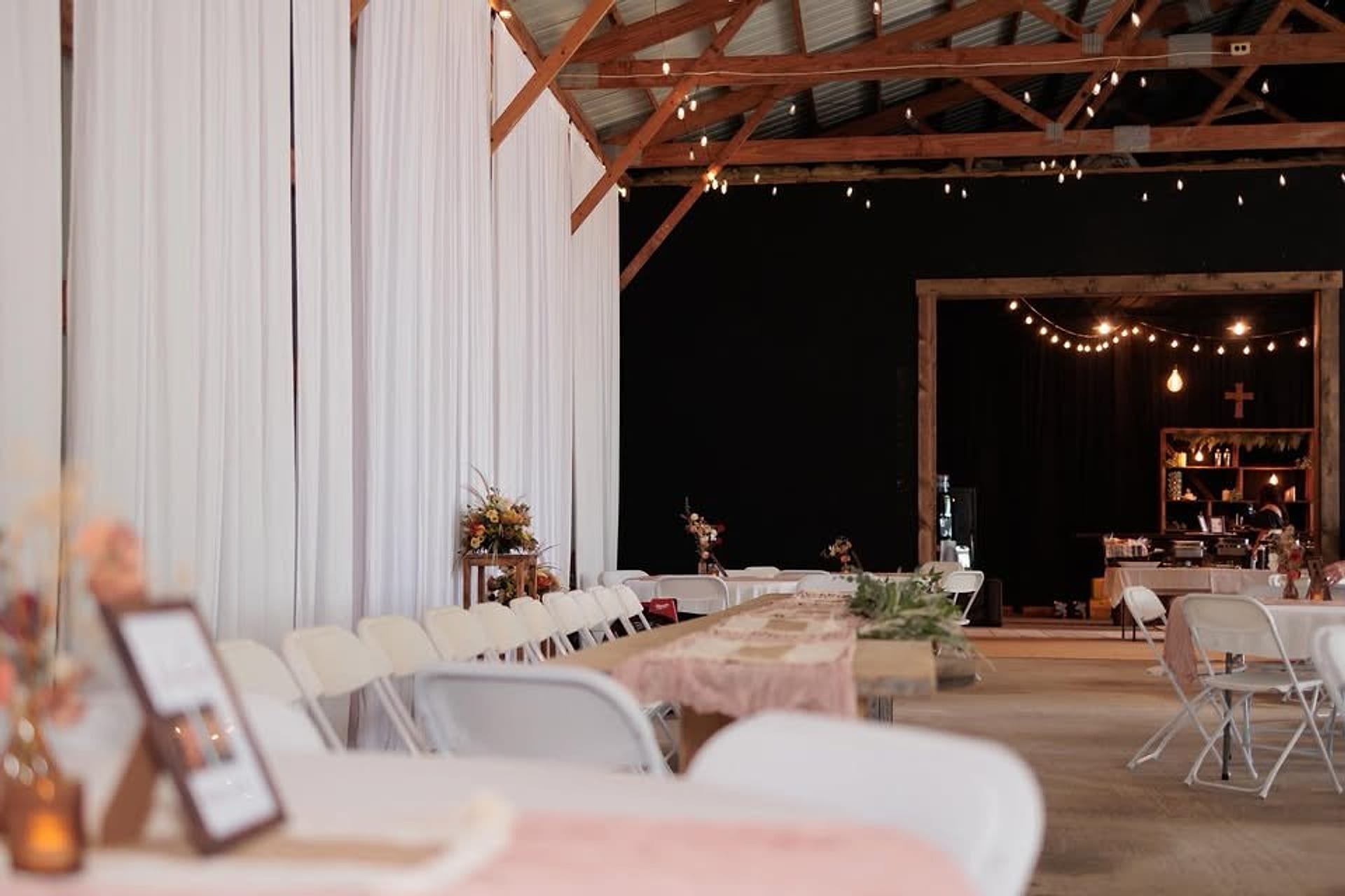 Inside the barn at Harvest Hollow: white draped walls, string lights overhead and tables set with blush linens