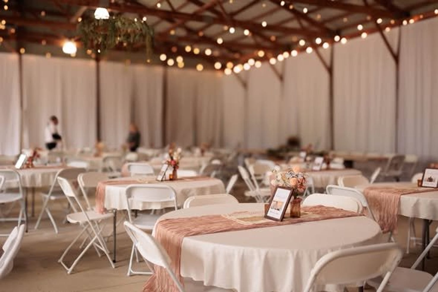 Round tables dressed in ivory and blush beneath strings of lights in the barn
